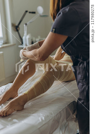 Professional cosmetologist woman removes all bandages after the procedure of wrapping in a beauty salon. Professional cosmetologist woman removes all bandages after the procedure of wrapping in a beauty salon. 117980278