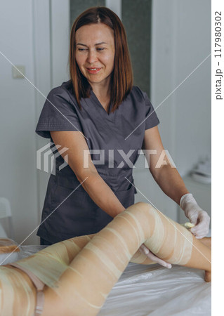 Professional cosmetologist woman removes all bandages after the procedure of wrapping in a beauty salon. Professional cosmetologist woman removes all bandages after the procedure of wrapping in a beauty salon. 117980302