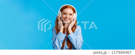 Waist-up shot cheerful pretty foxy caucasian girl listening music in large headphones, smiling pleased, checking-out friends single, wearing nightwear, standing blue background delighted Waist-up shot cheerful pretty foxy caucasian girl listening music in large headphones, smiling pleased, checking-out friends single, wearing nightwear, standing blue background delighted 117980467