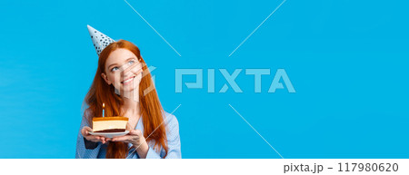 Dreamy, tender and feminine redhead caucasian girl thinking looking up thoughtful with tempting smile holding b-day cake pondering what wish make as blowing candle, celebrating birthday 117980620