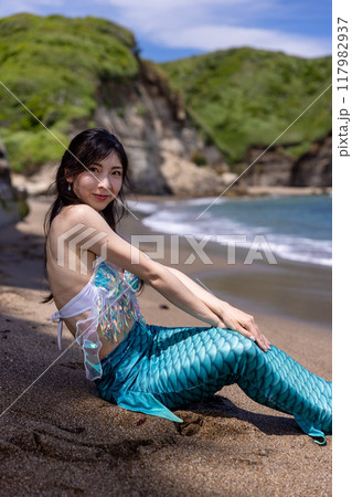 夏の海辺の砂浜に座って微笑む若い女性の人魚 117982937