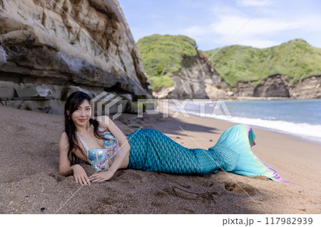 夏の海辺の砂浜の日陰に寝そべって微笑む若い女性の人魚 117982939