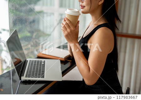 A woman enjoying coffee while working remotely from a modern, minimalist coffee shop. 117983667