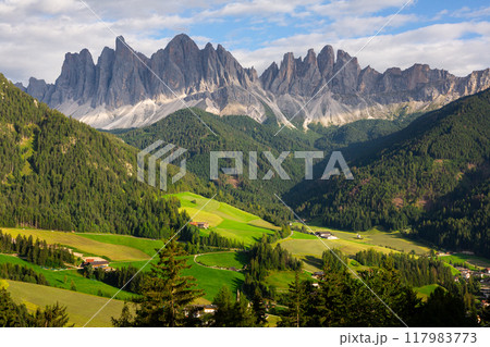 Alpine valley of Val di Funes with settlements surrounded by rocky Dolomites 117983773
