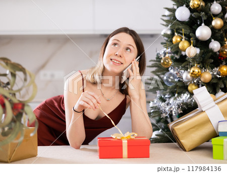 Attractive woman is preparing presents and discussing it with someone on a mobile phone Attractive woman is preparing presents and discussing it with someone on a mobile phone 117984136