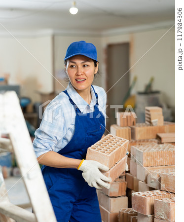 Female builder carrying bricks at renovating object 117984306