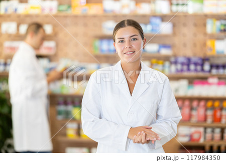 Young female pharmacist welcoming clients in chemist's shop 117984350