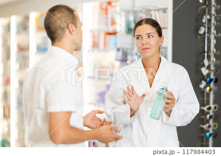 Female pharmacist consulting young guy about care product in bottle 117984403