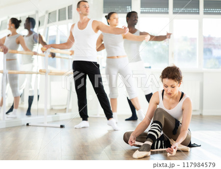 Female dancer adjusting point shoes on floor in ballet studio 117984579