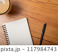 コーヒーラテが置かれたテーブルに開かれたノート 117984743