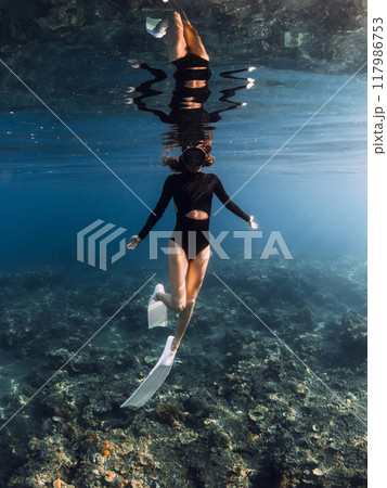 Woman freediver enjoys swimming in blue ocean on the reef. Vertical shot 117986753