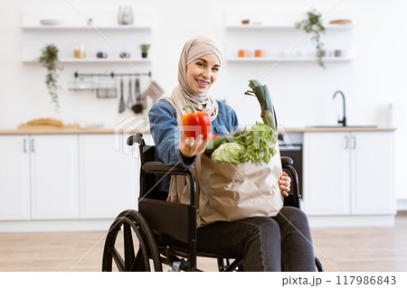 Muslim woman in wheelchair holding vegetables in modern kitchen Muslim woman in wheelchair holding vegetables in modern kitchen 117986843