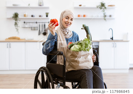 Muslim woman in wheelchair holding vegetables in modern kitchen 117986845