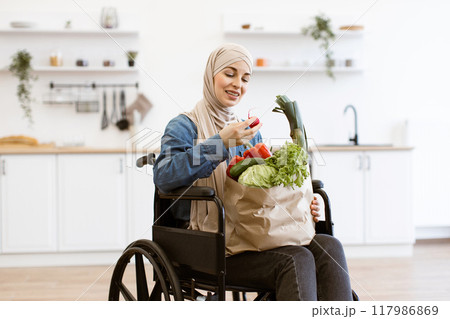 Muslim woman in wheelchair holding paper bag with fresh vegetables 117986869