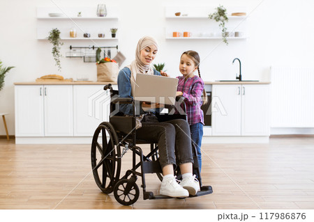 Woman with young girl using a laptop in kitchen 117986876