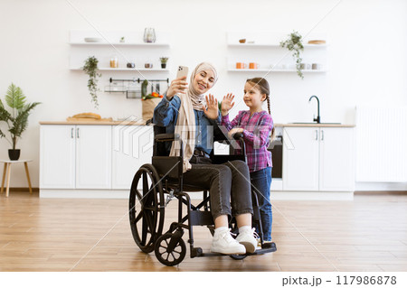 Muslim mother in wheelchair taking selfie with daughter in kitchen Muslim mother in wheelchair taking selfie with daughter in kitchen 117986878