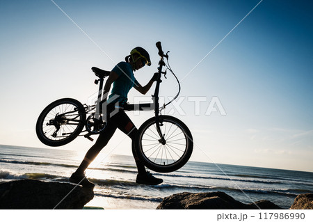 Woman taking a folding bike on sunrise seaside 117986990