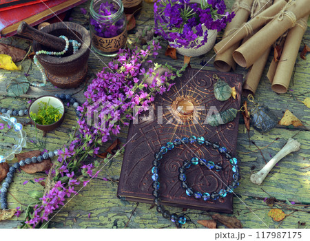 Mystic still life with magic book of spells, paper scrolls and witchy ritual objects on old table. Occult, esoteric, wicca and divination concept. No foreign language, all symbols are fictional 117987175