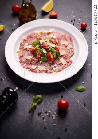 cooking tuna carpaccio - cherry tomato pieces on a plate with raw tuna fillet slices 117987722