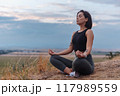 A serene woman meditates outdoors in nature at sunset, embracing tranquility and inner peace 117989559