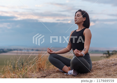 A serene woman meditates outdoors in nature at sunset, embracing tranquility and inner peace 117989559