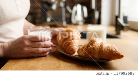 Girl with milk and croissants for breakfast Girl with milk and croissants for breakfast 117992698
