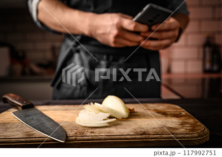 Chief with smartphone and onion at kitchen Chief with smartphone and onion at kitchen 117992751