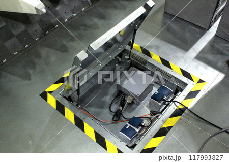 An open metal floor hatch revealing a panel of electrical components and wiring, providing access to essential industrial infrastructure 117993827