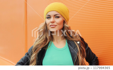 Portrait beautiful young blonde woman posing in black leather jacket on colorful orange background Portrait beautiful young blonde woman posing in black leather jacket on colorful orange background 117994365