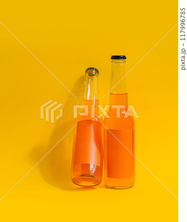 Two orange soda bottles leaning against yellow background 117996785