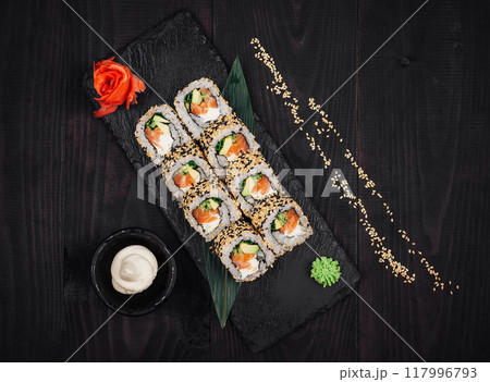 Sushi rolls set served on black stone plate on dark wooden table 117996793