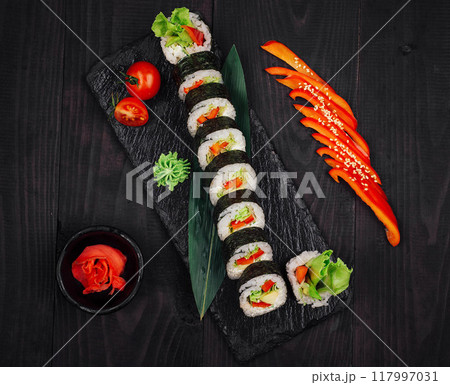 Sushi rolls laid out on black slate platter with red pepper and wasabi 117997031