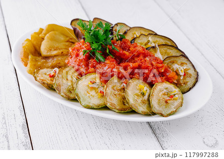 Grilled eggplant and zucchini slices lying on plate with tomato salsa and parsley 117997288