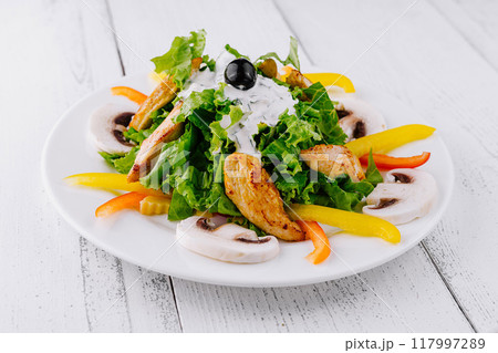 Delicious salad with grilled chicken, mushrooms and yogurt dressing on white wooden table 117997289