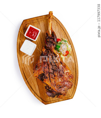 Roasted lamb shank with vegetables and sauces on wooden board 117997338