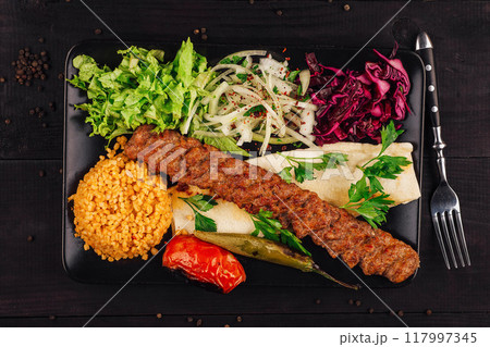 Traditional adana kebab serving with bulgur, salad and lavash bread on black plate Traditional adana kebab serving with bulgur, salad and lavash bread on black plate 117997345
