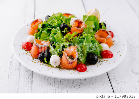 Delicious salad with smoked salmon, mozzarella and cherry tomatoes on white table Delicious salad with smoked salmon, mozzarella and cherry tomatoes on white table 117998018
