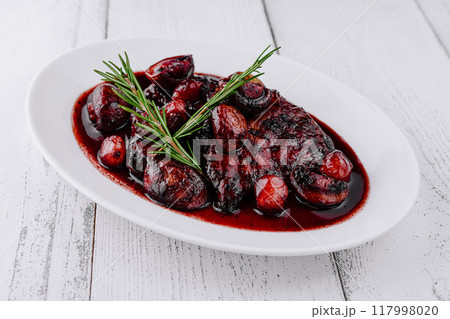 Delicious duck breast covered in cherry sauce with rosemary sprig on white plate 117998020