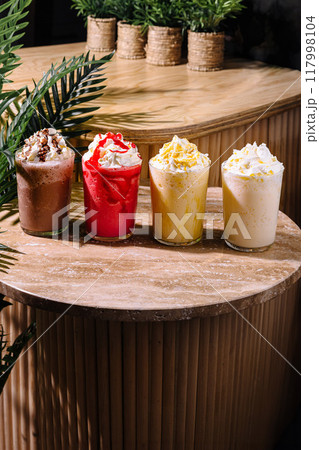 Four colorful milkshakes topped with whipped cream sitting on a stone table 117998104