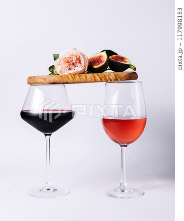 Two glasses with red and rose wine balancing wooden board with ripe figs and pink rose 117998183