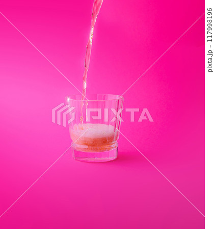 Pink drink being poured into a glass on a pink background 117998196