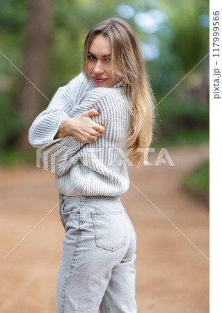 Beautiful blonde woman hugging herself outdoors in a park 117999566