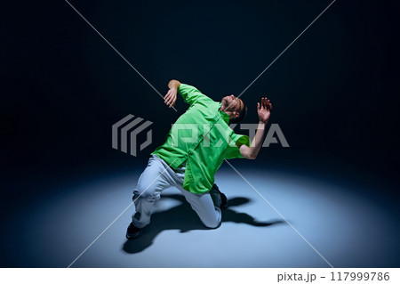 Flexible, artist, talented young guy in casual clothes making dynamic performance on stage, dancing hip-hop against black studio background 117999786
