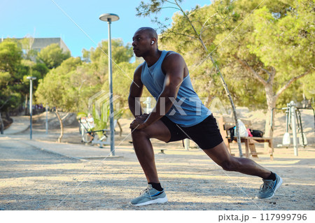 African athletic man do leg stretching exercises outdoors 117999796