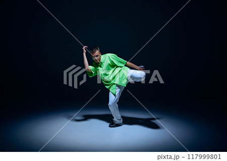 Young guy in jeans and green t-shirt dancing hip-hop with energy and rhythm against black studio background Young guy in jeans and green t-shirt dancing hip-hop with energy and rhythm against black studio background 117999801
