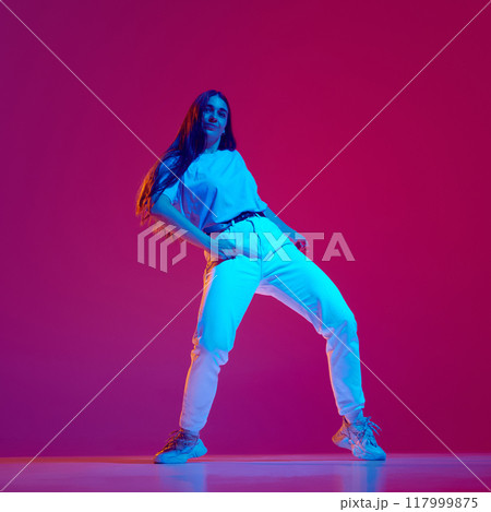 Artistic, energetic and expressive young woman in casual clothes in motion, dancing hip-hop against magenta, pink background in neon light Artistic, energetic and expressive young woman in casual clothes in motion, dancing hip-hop against magenta, pink background in neon light 117999875
