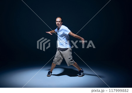 Dynamic image of artistic young man in casual clothes dancing hip-hop on stage against black studio background with spotlight Dynamic image of artistic young man in casual clothes dancing hip-hop on stage against black studio background with spotlight 117999882