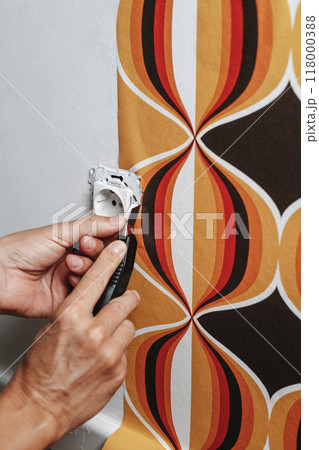 cuts the edges of the wallpaper surrounding a socket 118000388