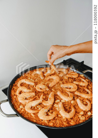 man ads some shrimps to the fideua, a noodle paella man ads some shrimps to the fideua, a noodle paella 118000392