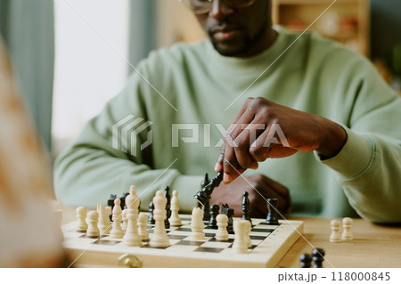 Hand of young African American man moving queen piece during chess game with unrecognizable friend Hand of young African American man moving queen piece during chess game with unrecognizable friend 118000845